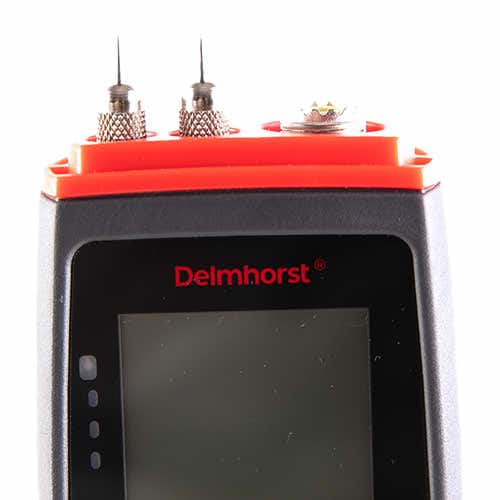 Close-up of the Delmhorst BDX-30 moisture meter top showing the two measuring pins, contact connector and red pin cap above the display bezel.